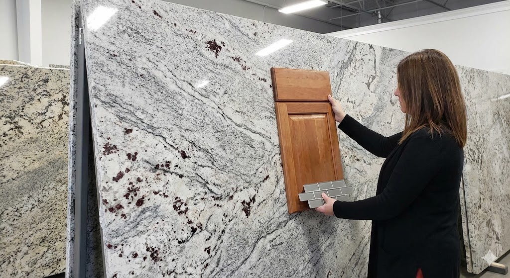 A customer in a stone showroom holding a wood cabinet door sample and a gray subway tile sample against a large, dramatic slab of New River White granite to check color compatibility before purchase.
