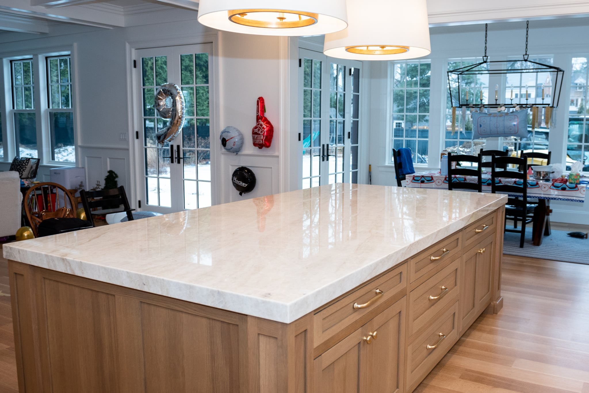 Large kitchen island featuring polished Taj Mahal quartzite countertops on a natural wood base with brass hardware in a Needham, MA home.