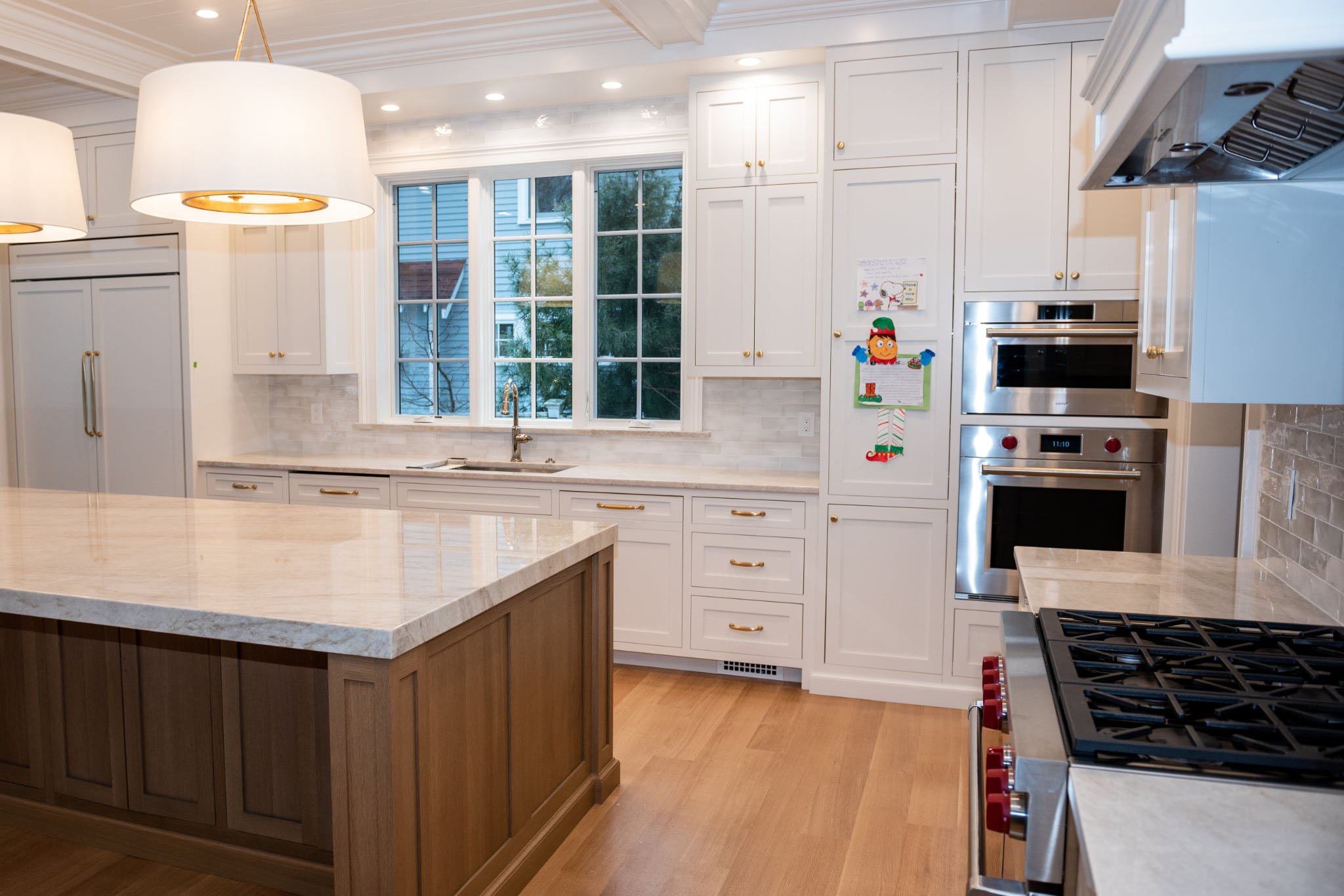 Spacious Needham kitchen featuring polished Taj Mahal quartzite countertops paired with white shaker cabinets and stainless steel appliances.