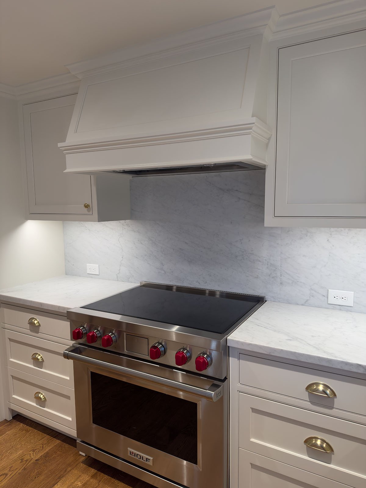  White Carrara marble countertop and full-height backsplash behind professional range with white cabinets and brass hardware, Weston Massachusetts