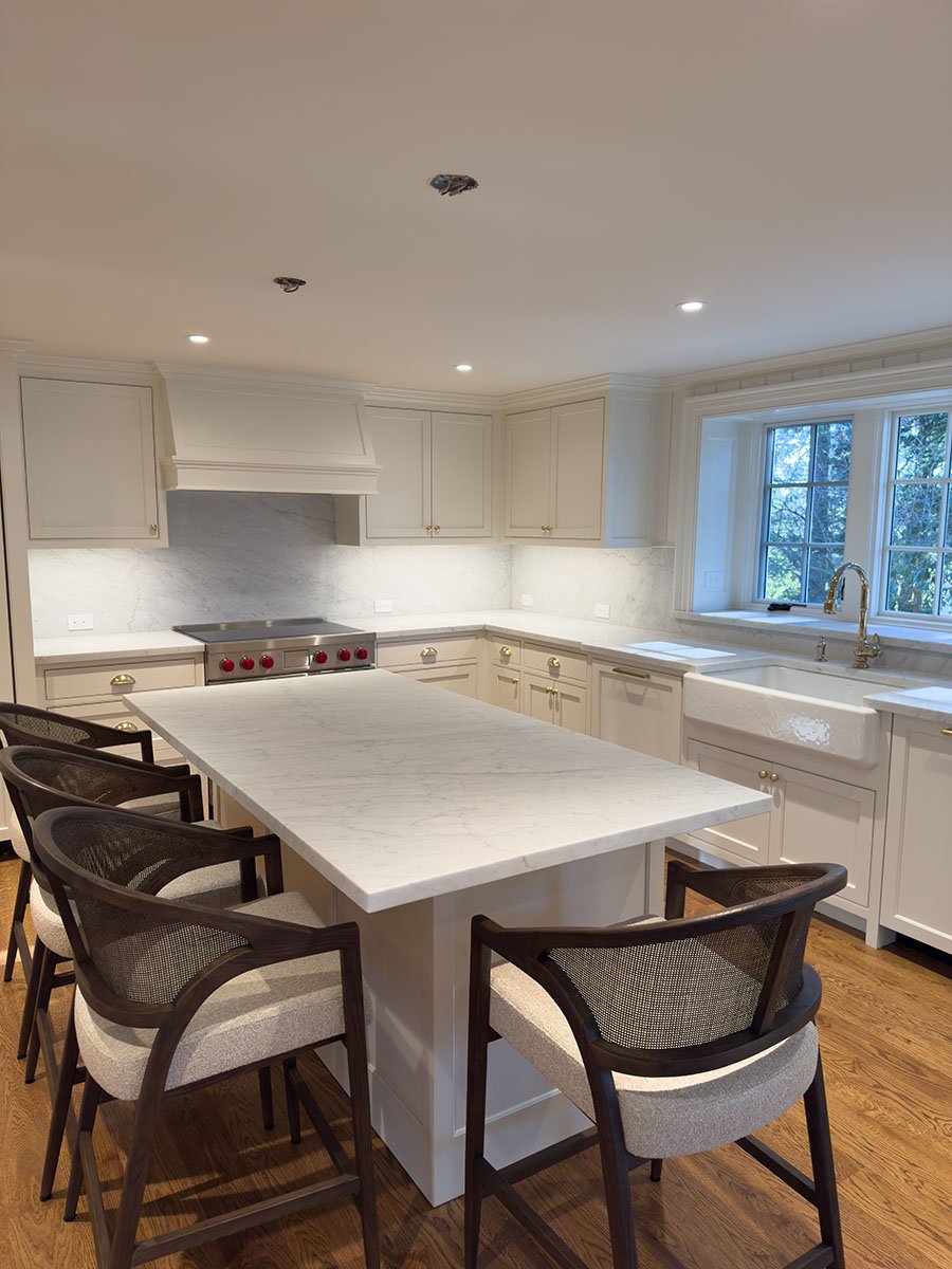 White Carrara marble kitchen with large island, full backsplash, farmhouse sink, and white cabinets, Weston Massachusetts