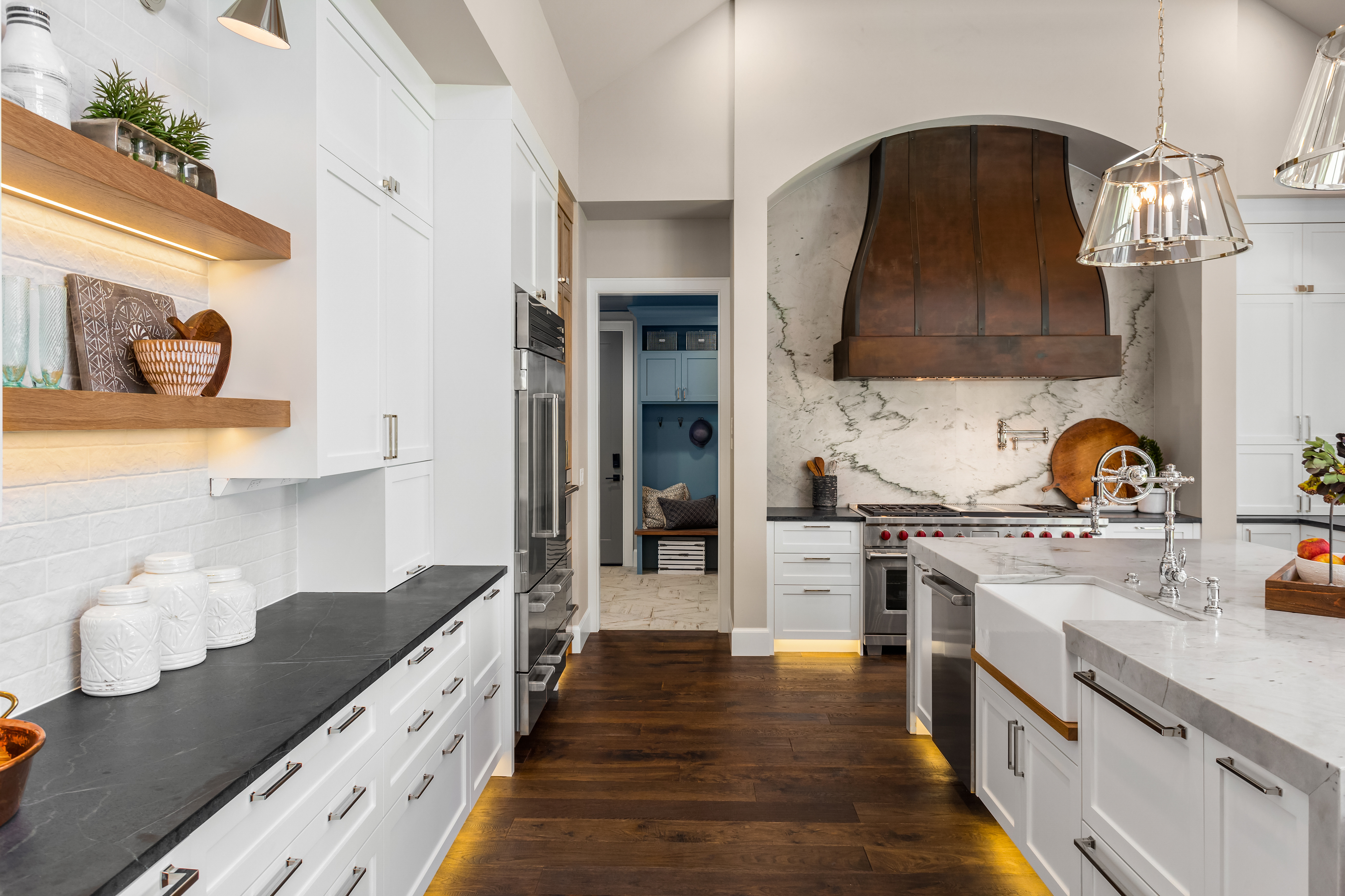 Luxury kitchen with white shaker cabinets, marble backsplash, and dark granite countertops, featuring a farmhouse sink and custom range hood. Granite Guy Inc.